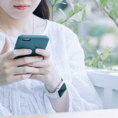 woman in white and blue floral dress holding green smartphone